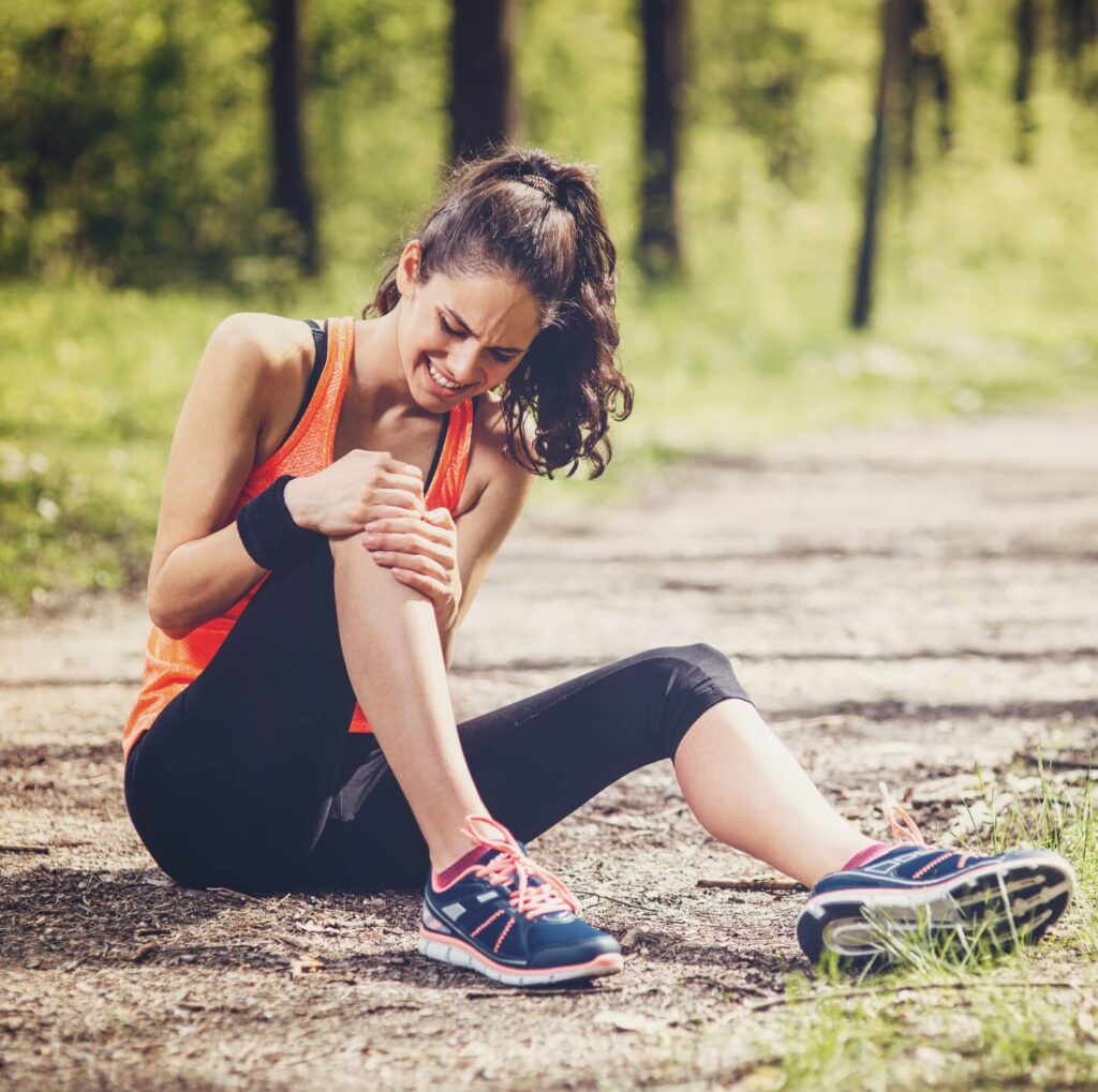 Woman sitting on the ground holding her knee with a possible MCL injury.