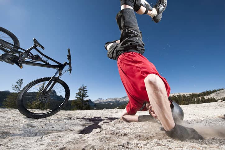 Mountain biker in red shirt flips on his head breaking his clavicle, which is the most common mountain bike injury.