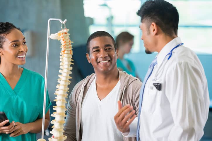 Doctor with spine model talking to smiling couple giving a spinal patient testimonial.