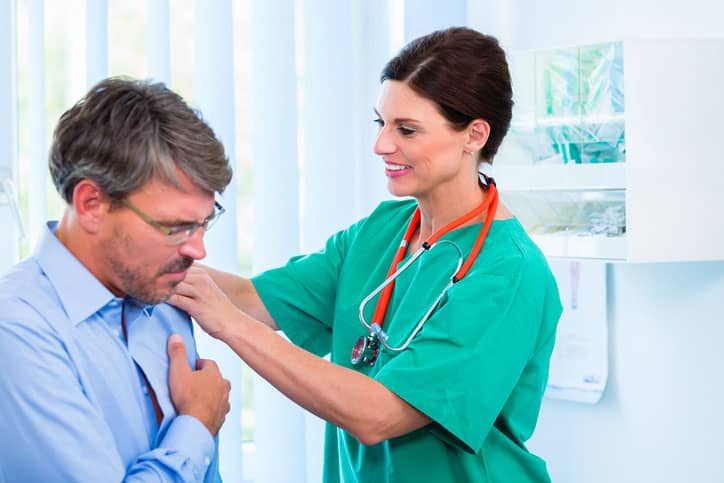 Patient in blue shirt being given a shoulder checkup by a nurse after total shoulder replacement.